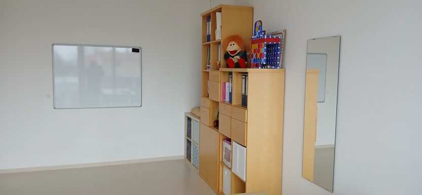 Raum 2: Heller Raum mit Bücherregal, Spiegel und einem weißen Wandboard.