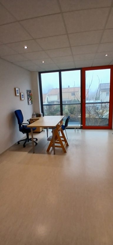 Raum 2: Moderner Büroraum mit Tisch, zwei Stühlen und großen Fenstern.