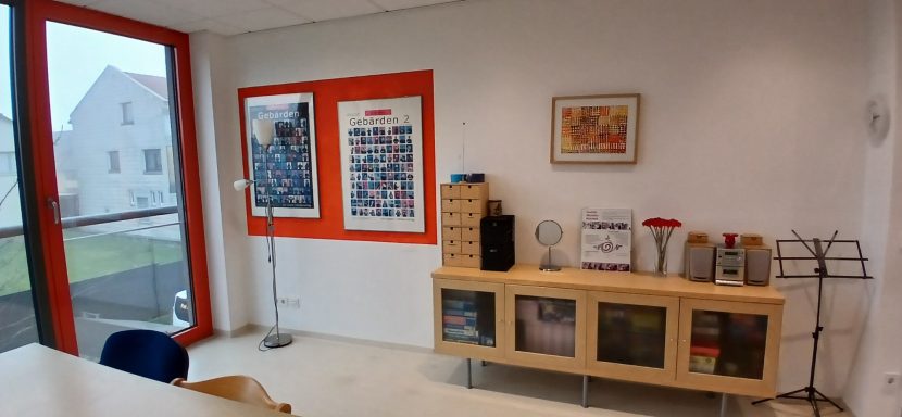 Raum 2: Büro mit Holzregal, Kunstwerken an der Wand und Sitzgelegenheit.